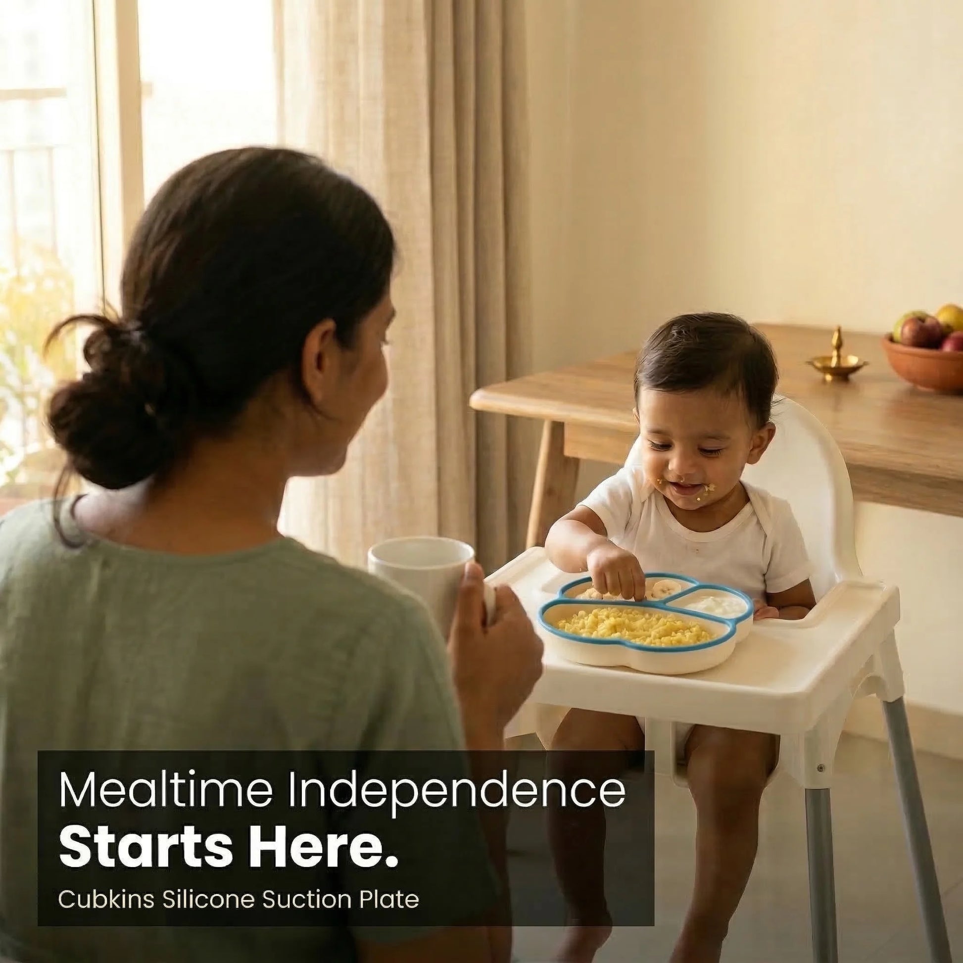 Indian mother watching her baby self-feed happily from blue Cubkins silicone suction plate on highchair — mealtime independence lifestyle photo