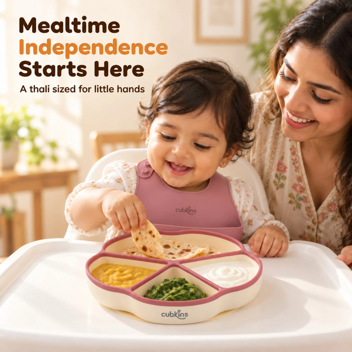 Indian mother smiling as her baby feeds himself from the Cubkins raspberry silicone suction plate on a high chair
