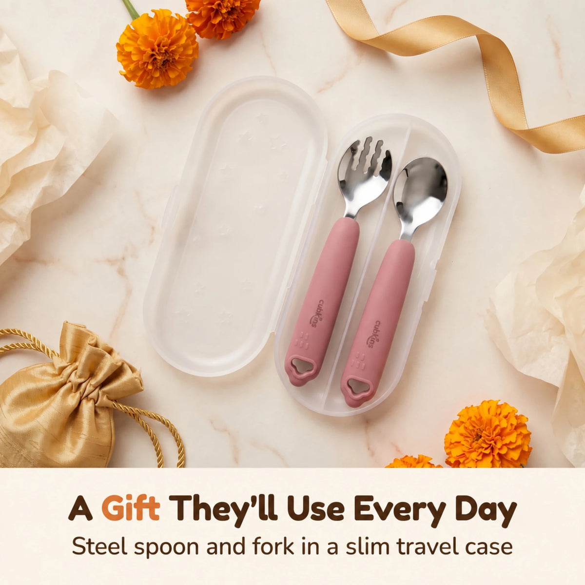 Cubkins raspberry steel toddler spoon and fork in an open travel case, styled as a gift with marigolds, gold ribbon and a silk potli pouch