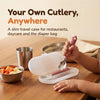 Toddler lifting the Cubkins raspberry steel spoon out of its open travel case at a restaurant table beside a steel katori of fruit
