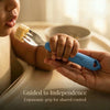 Close-up of a baby and parent's hands both holding a Cubkins Blue Olive toddler fork as the baby brings a piece of banana to their mouth, with the caption "Guided to Independence – Ergonomic grip for shared control"