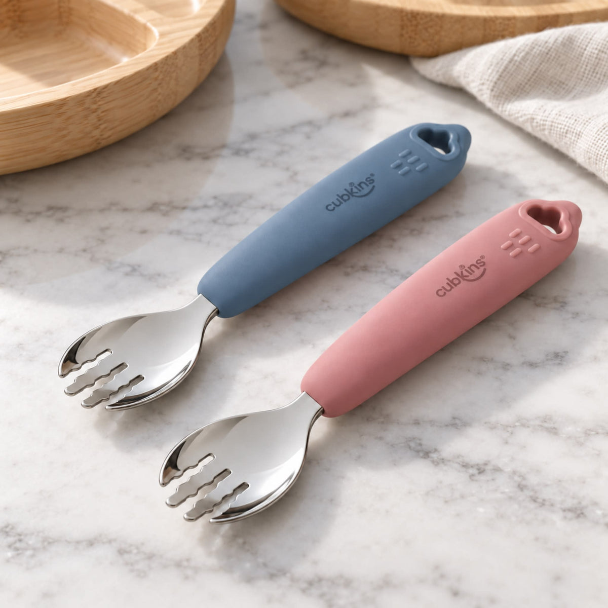 Two Cubkins stainless steel toddler forks, one raspberry and one blue olive silicone handle, on a marble counter, set of 2