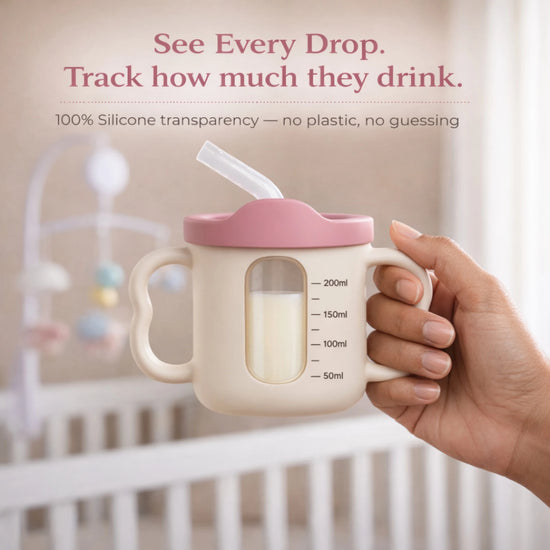 Adult hand holding the Cubkins raspberry pink silicone straw training cup showing the transparent window with measurement markings from 50ml to 200ml to track how much baby drinks