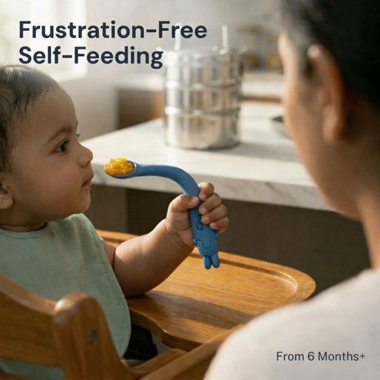 Indian baby from 6 months self-feeding with Cubkins blue bendable silicone spoon in a wooden high chair, with parent watching