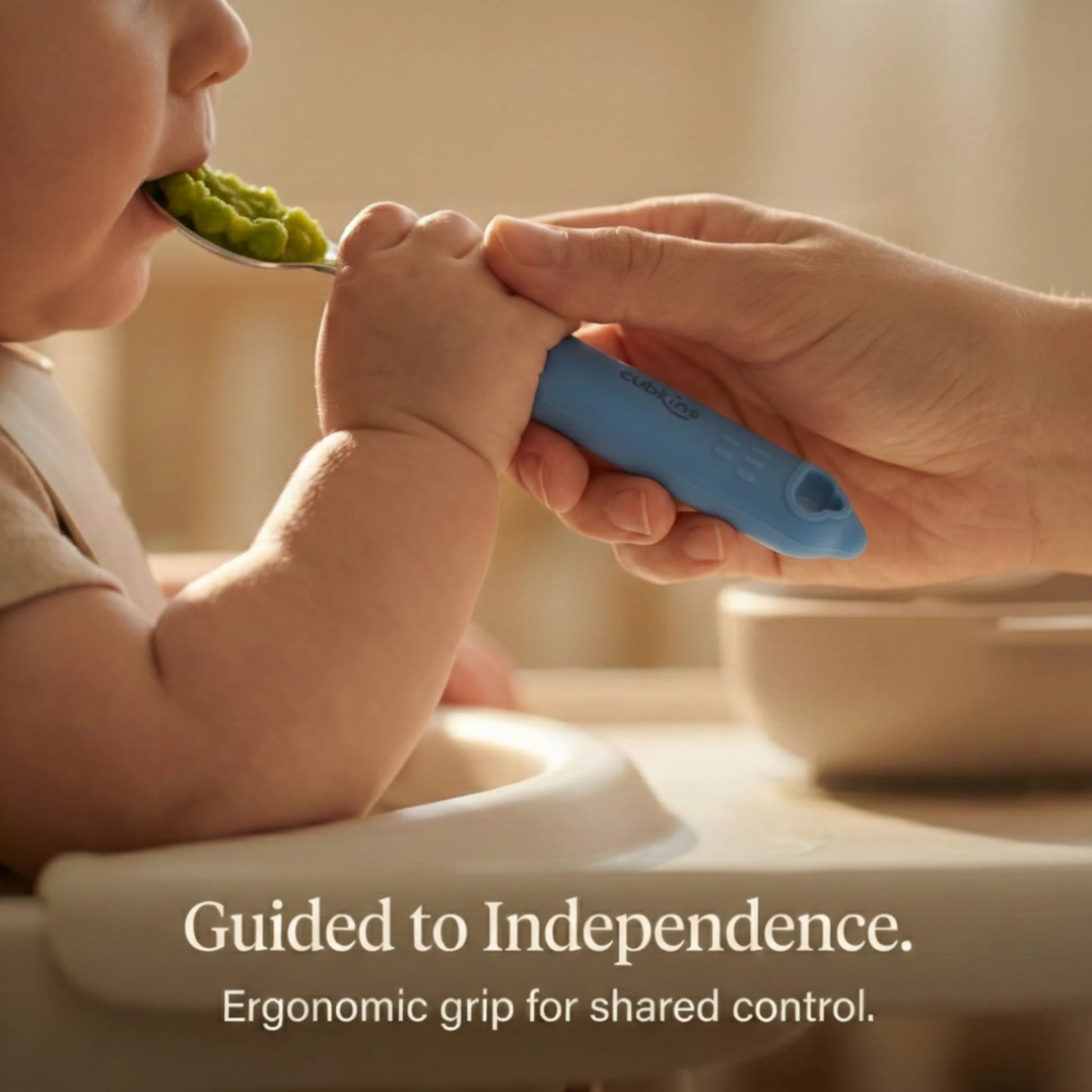 Mother's hand guiding a baby's grip on the Cubkins ergonomic silicone spoon handle to encourage independent eating.