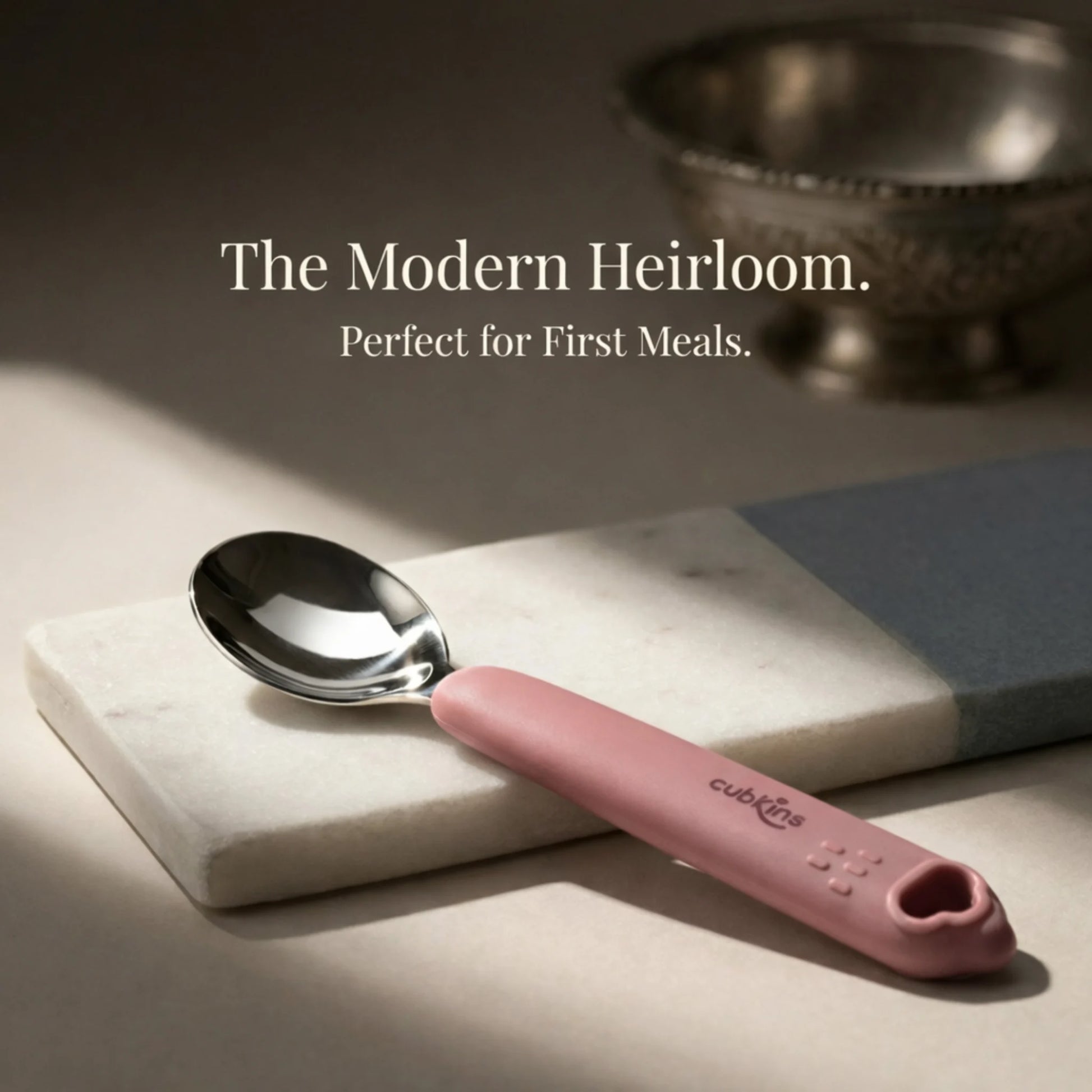 Cubkins stainless steel baby spoon with raspberry pink silicone handle on a marble slab; ideal for baby's first meals.