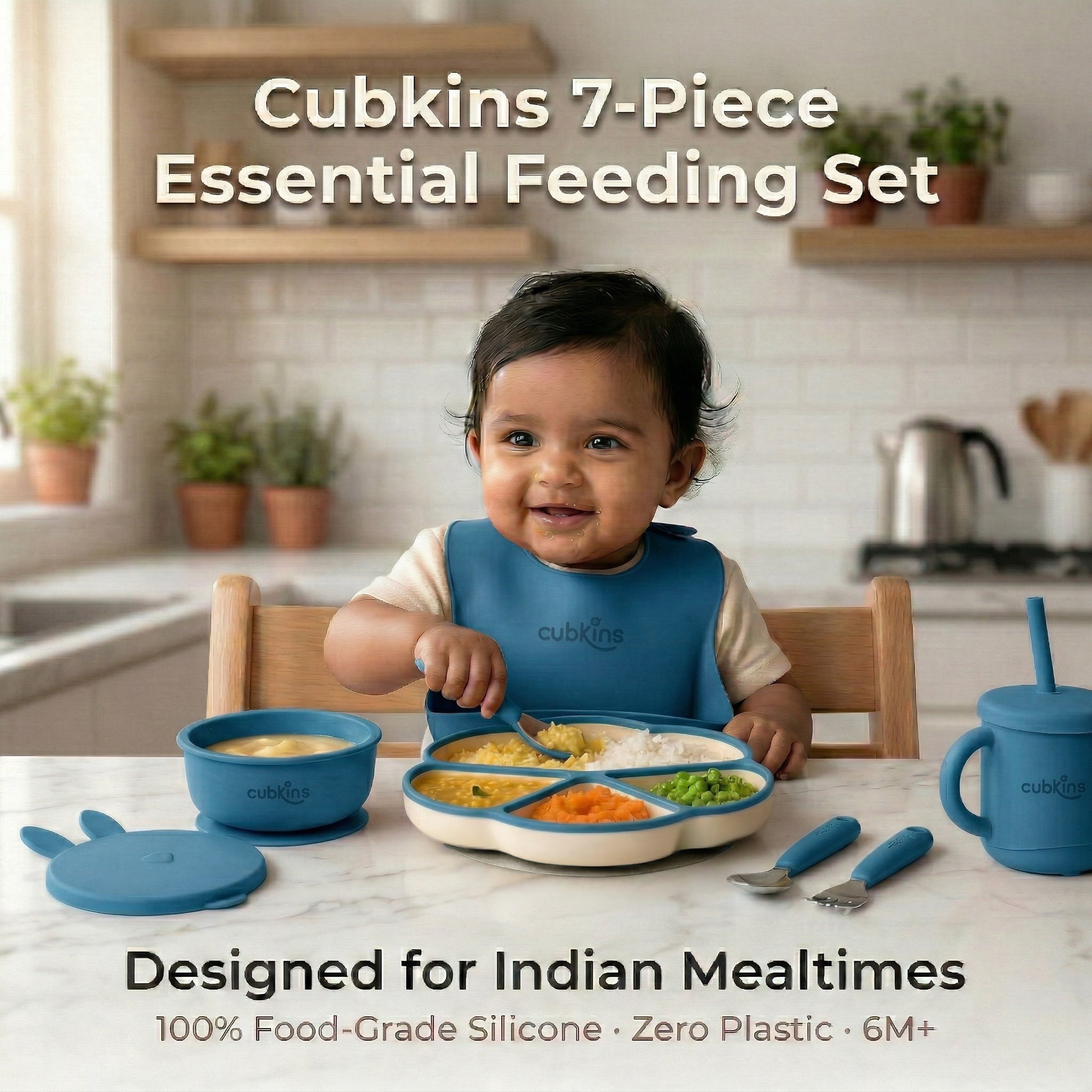 Smiling baby in a blue Cubkins silicone bib sitting at a marble kitchen counter with the full 7-piece Essential Feeding Set in blue — divided suction plate, suction bowl with bunny lid, straw sippy cup, and stainless steel cutlery — filled with dal, rice, and vegetables.