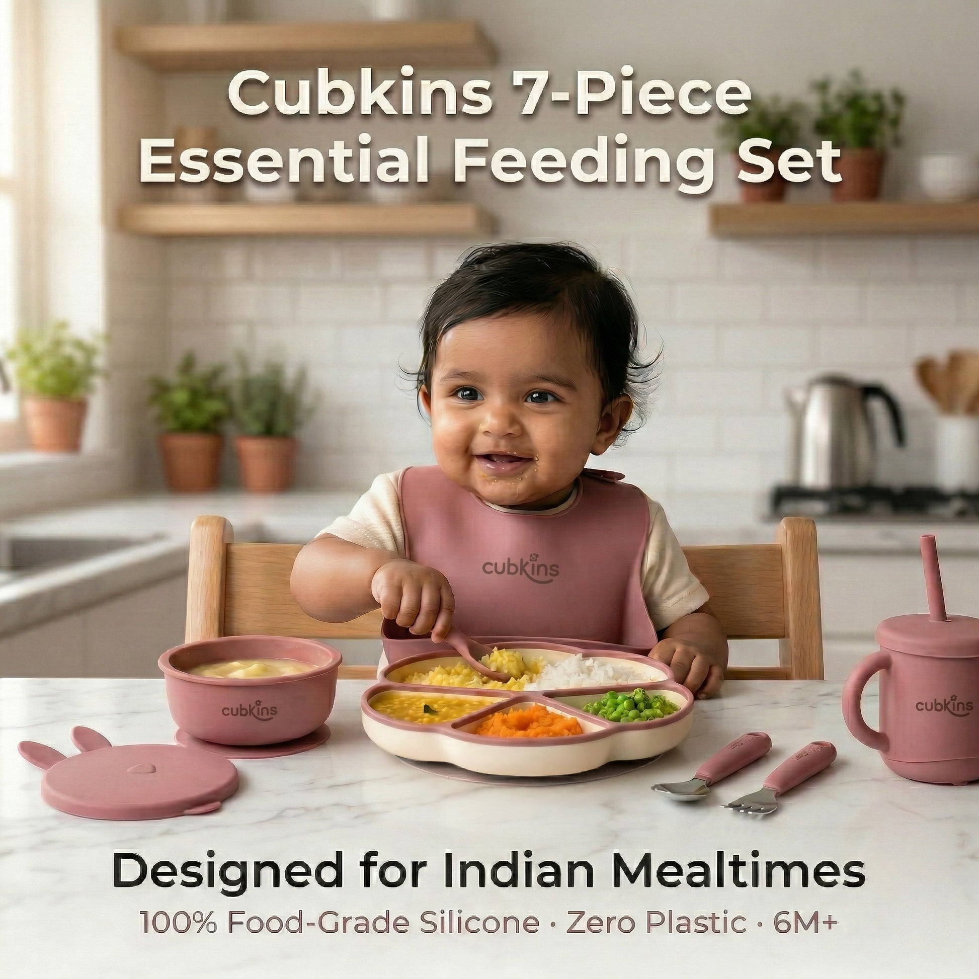 Smiling baby in a raspberry Cubkins silicone bib sitting at a marble kitchen counter with the full 7-piece Essential Feeding Set in raspberry — divided suction plate, suction bowl with bunny lid, straw sippy cup, and stainless steel cutlery — filled with dal, rice, and vegetables.