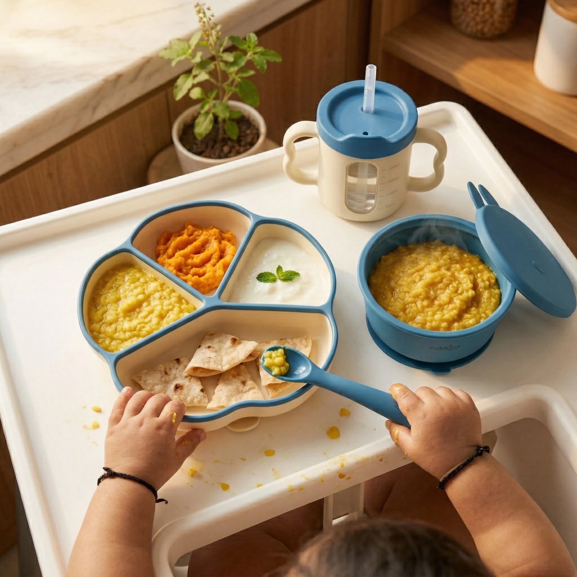 Indian baby eating khichdi, roti, and dal using Cubkins Blue Silicone Divided Plate, Suction Bowl, and Sippy Cup on high chair tray