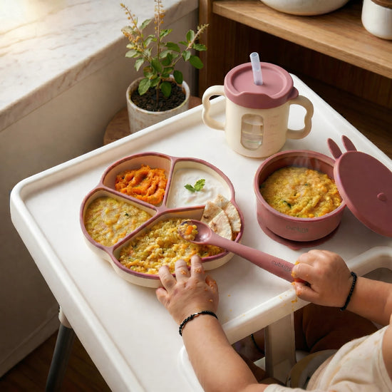 Baby self-feeding khichdi and dal with Cubkins Raspberry Silicone Divided Plate, Suction Bowl with Lid, and Sippy Cup on high chair tray