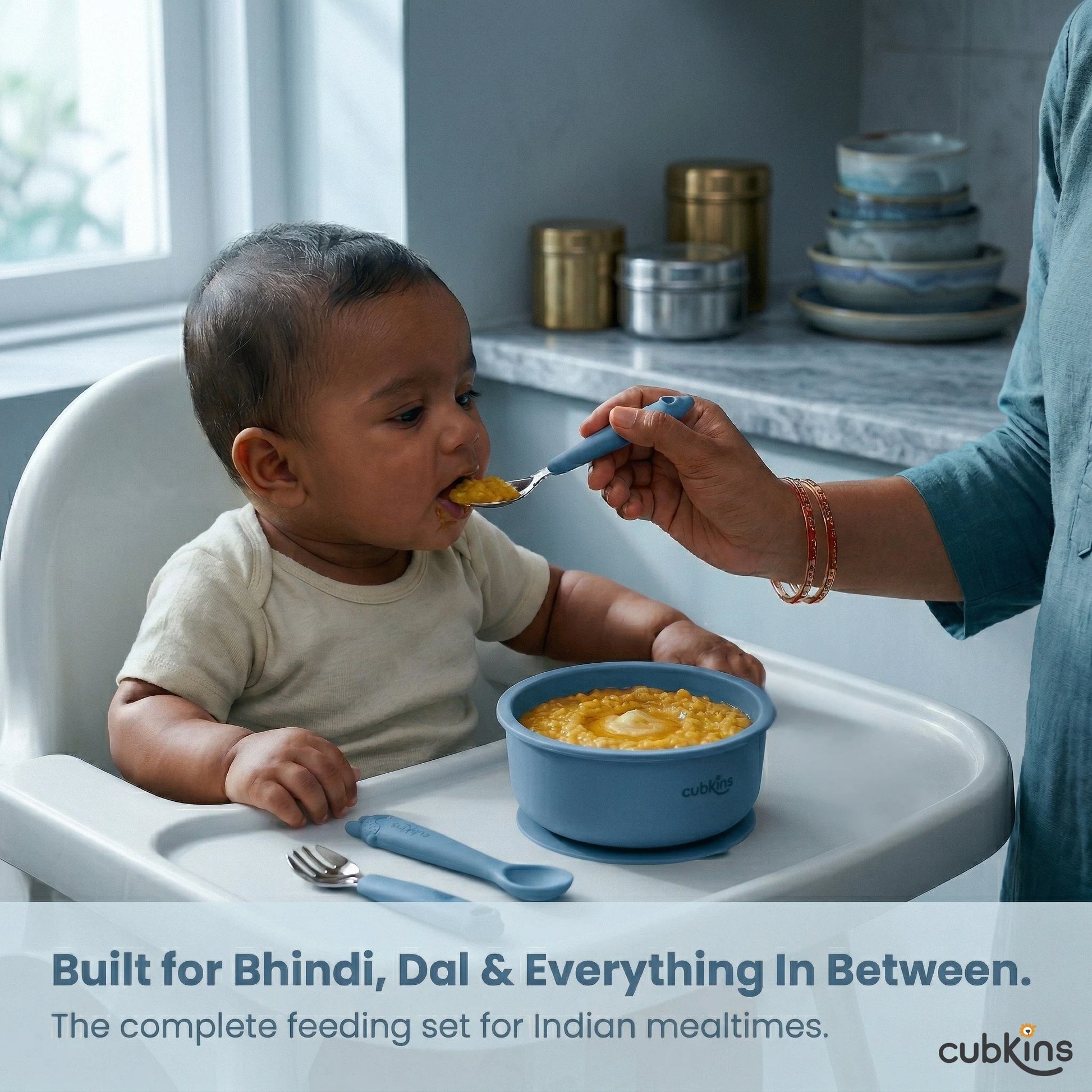 Indian mother feeding baby dal khichdi in high chair using Cubkins blue stainless steel spoon – complete feeding set for Indian mealtimes