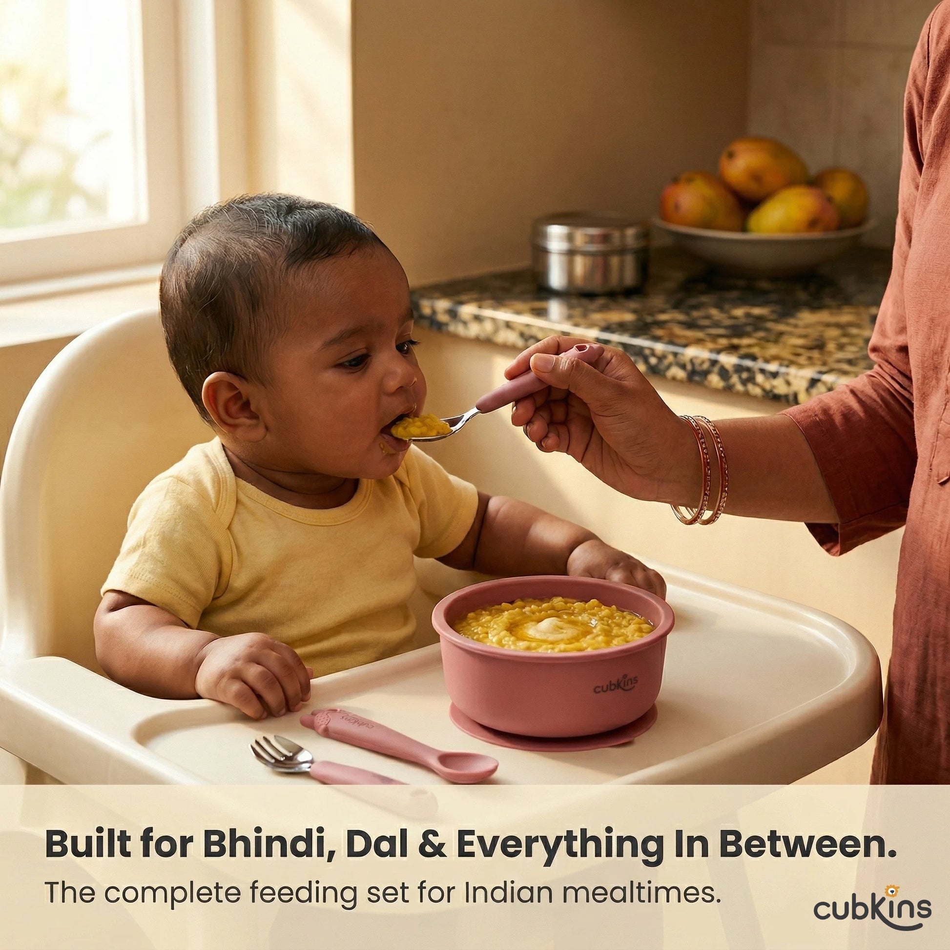 Indian mother feeding baby dal khichdi in high chair using Cubkins raspberry stainless steel spoon – baby feeding set built for Indian foods