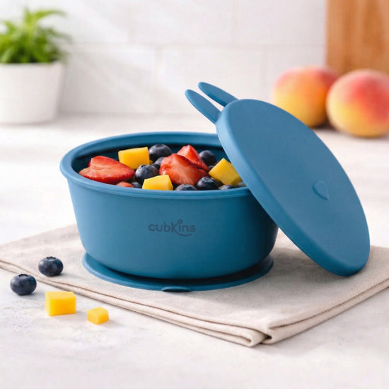 Cubkins blue silicone suction bowl with bunny ear lid filled with fresh fruit including strawberries, blueberries, and mango on kitchen counter