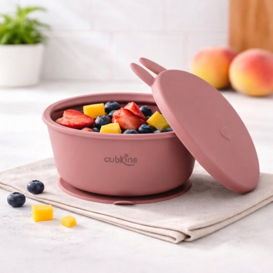 Cubkins raspberry pink silicone suction bowl with bunny ear lid filled with fresh fruit including strawberries, blueberries, and mango on kitchen counter